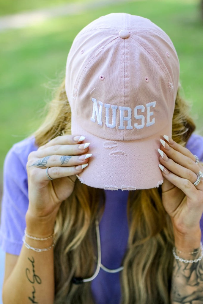 Rose colored distressed baseball cap with "NURSE" in white block letters
