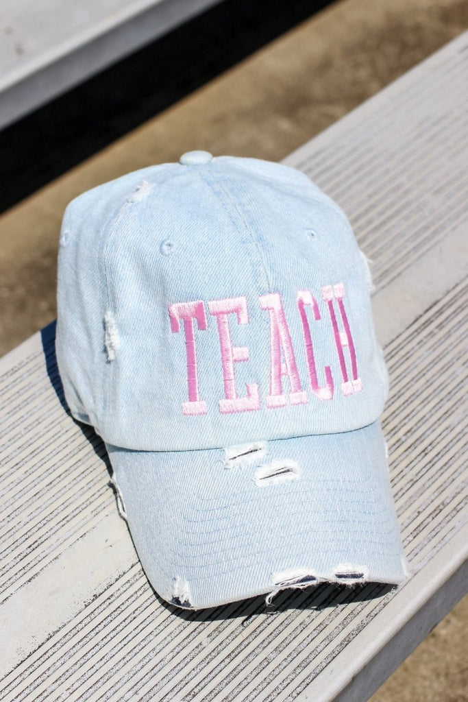 Light denim distressed adjustable baseball hat with light pink stitching with TEACH in block letters